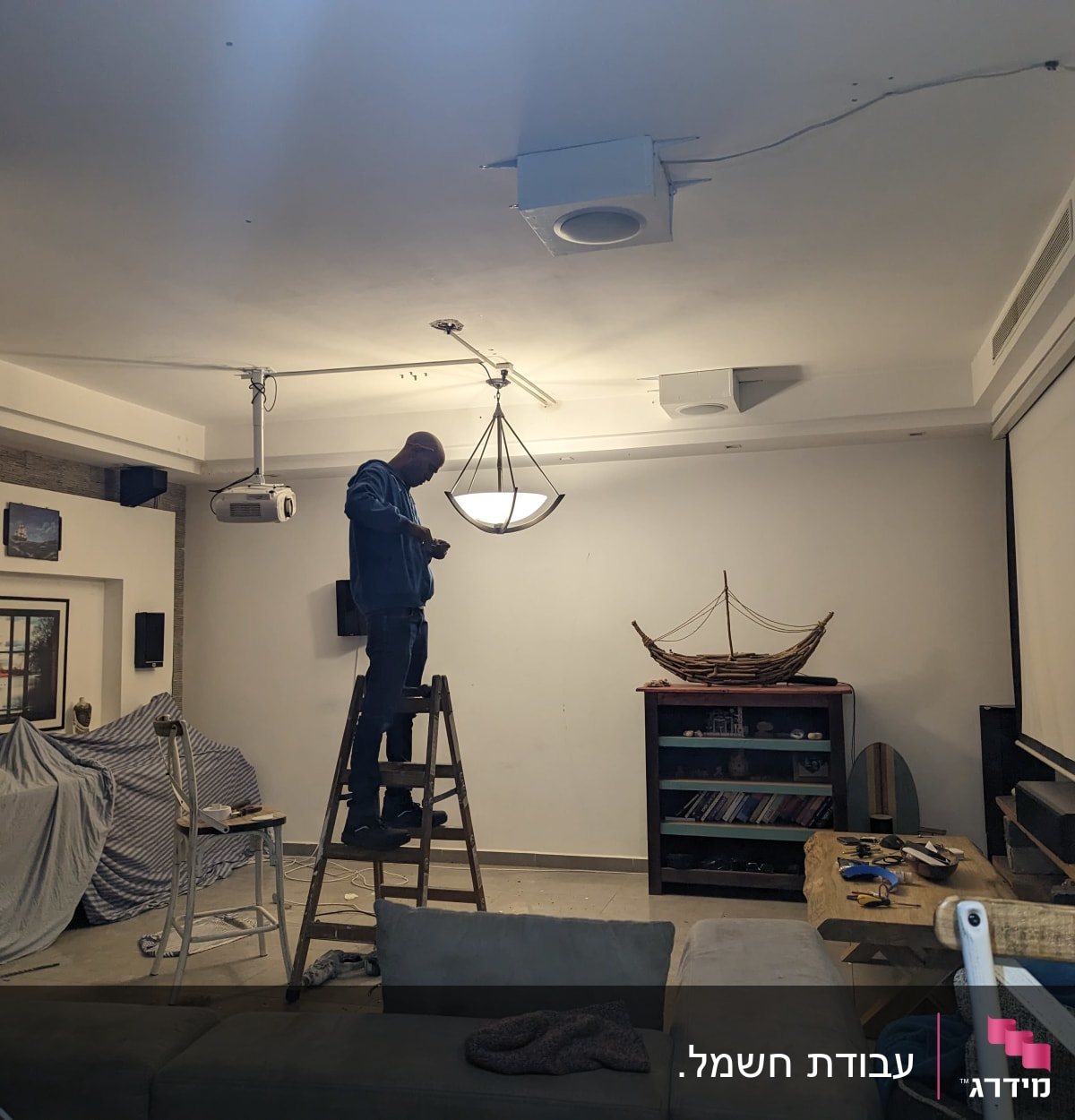 חשמלאי עומד על סולם ומתקן מנורה בתקרה